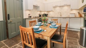 Una cocina moderna con armarios blancos, una mesa de comedor con platos y vasos azules, y un suelo de baldosas de piedra.