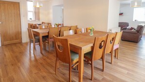 A spacious dining area with a wooden table and chairs, a vase with flowers, and a brown leather sofa in the background. - The Bull Inn (Caernarfon)