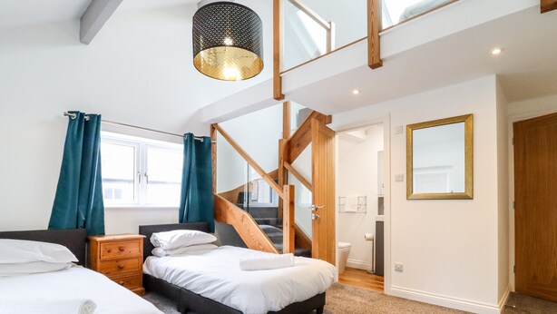 A bedroom with two beds, a wooden staircase, a bathroom, and a large window. - The Bull Inn (Caernarfon)