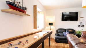 A living room with a foosball table, a leather sofa, a TV, and a ship model on the wall. - The Bull Inn (Caernarfon)