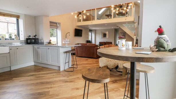 A modern kitchen with a central island, a dining area with a round table, and a loft space with a staircase. - Pheasant's Roost (Hull)