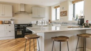 A modern kitchen with white cabinets, a large island with stools, a stove, and a window with a view. - Pheasant's Roost (Hull)