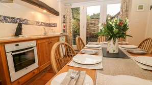 A modern kitchen with a Bosch oven, wooden cabinets, and a dining area set for four with a large vase of flowers. - End Cottage (Skipton)