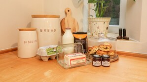 A kitchen counter with various food items and kitchenware, including jars labeled 'BREAD', 'BISCUITS', and 'DIALS DAILIES', along with a plant and a window in the background. - End Cottage (Skipton)