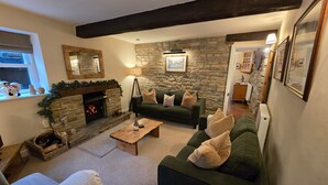 A cozy living room with a stone fireplace, green sofa, and a wooden coffee table. - End Cottage (Skipton)