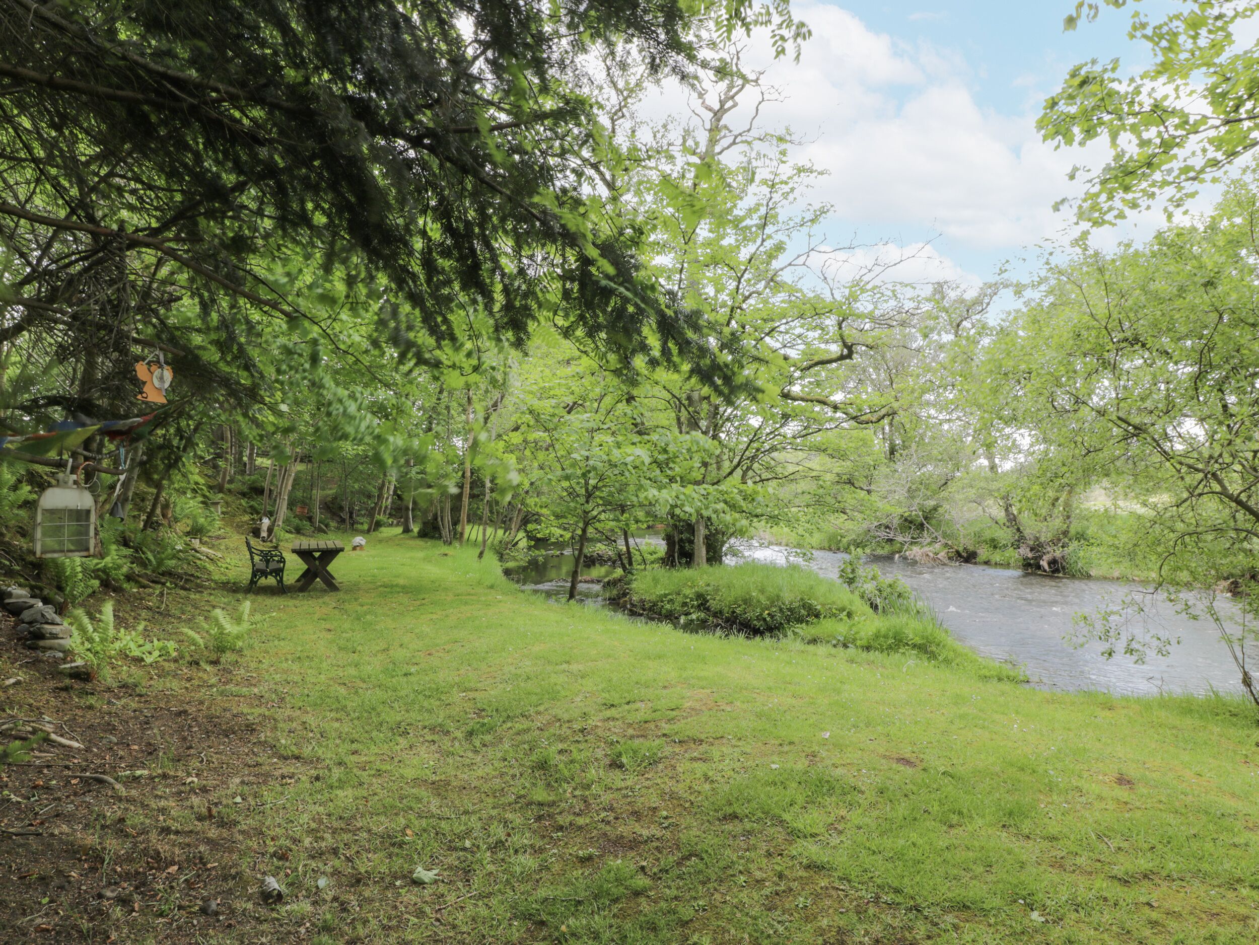 A serene park with a picnic table and benches, a small stream, and lush greenery.