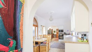 A cozy dining area with wooden chairs and a table, a kitchen with a refrigerator and oven, and a colorful curtain. - Torview House (Peebles)