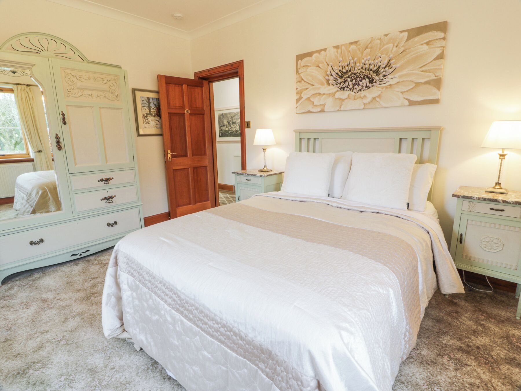 Une chambre à coucher avec un grand lit, une commode, un miroir et un tableau accroché au mur.