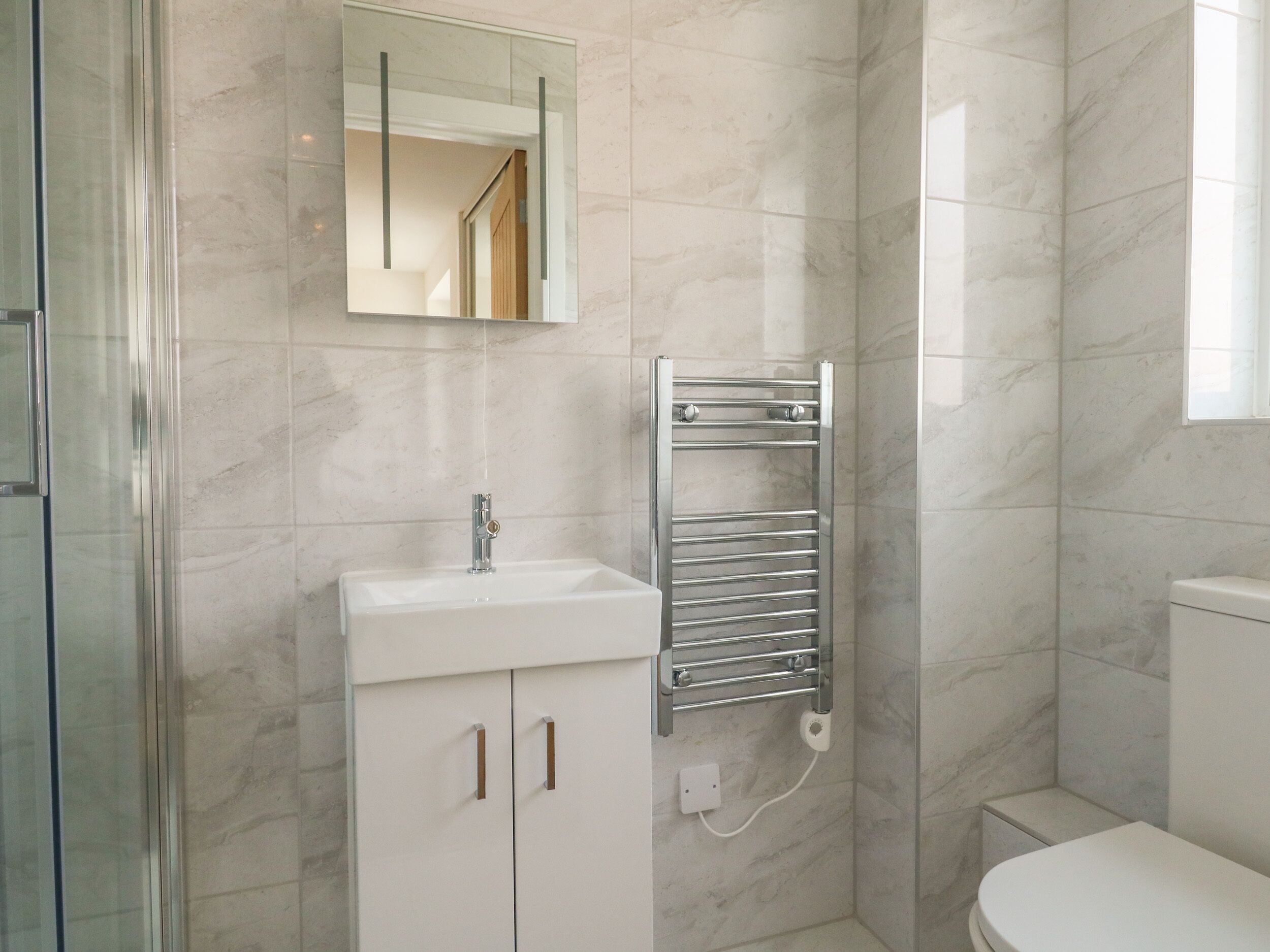 A modern bathroom with a glass shower enclosure, a white sink with a mirror above, and a toilet.
