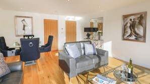 Ein Wohnzimmer mit grauem Sofa, einem Glastisch und einem Essbereich mit Tisch und Stühlen.
