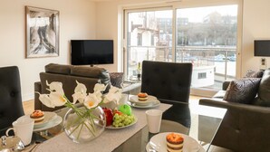 Ein modernes Wohnzimmer mit großem Fenster, einem Flachbildfernseher und einem Essbereich mit Tisch für zwei Personen.