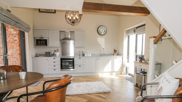 A modern kitchen with white cabinets, a stainless steel range hood, and a built-in oven. There is a dining area with a wooden table and leather chairs. - Owl's Hoot (Hull)