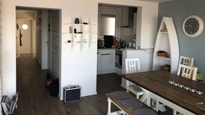 Une cuisine compacte avec des étagères blanches, une table à manger avec des tabourets et une horloge au mur.