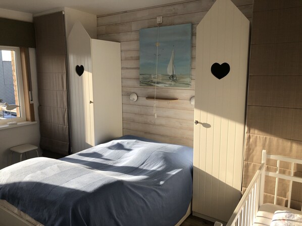 A bedroom with a bed, a window, a painting of a sailboat, and two doors with heart-shaped cutouts. - Seafront, 95 m2 5th floor apartment, 3 bedrooms, Wi-fi, Garage, Terrace (Koksijde)