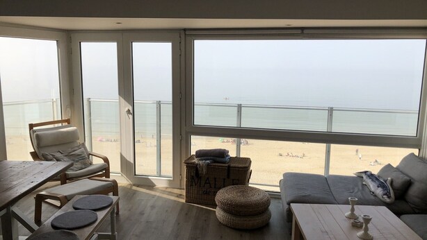 Une pièce dotée d’une grande fenêtre donnant sur une plage, avec un canapé, une table et une chaise.