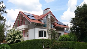 A two-story house with a red-tiled roof, solar panels, and a gated entrance.
