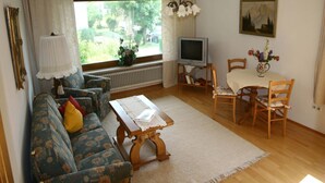A living room with a sofa, a coffee table, a TV, and a dining table with chairs.