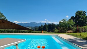A swimming pool with two glasses of red wine on a table, surrounded by greenery and mountains in the background. - Five-star comfort vacation apartment Sternenstadl with balcony allergy-friendly (Rimsting)
