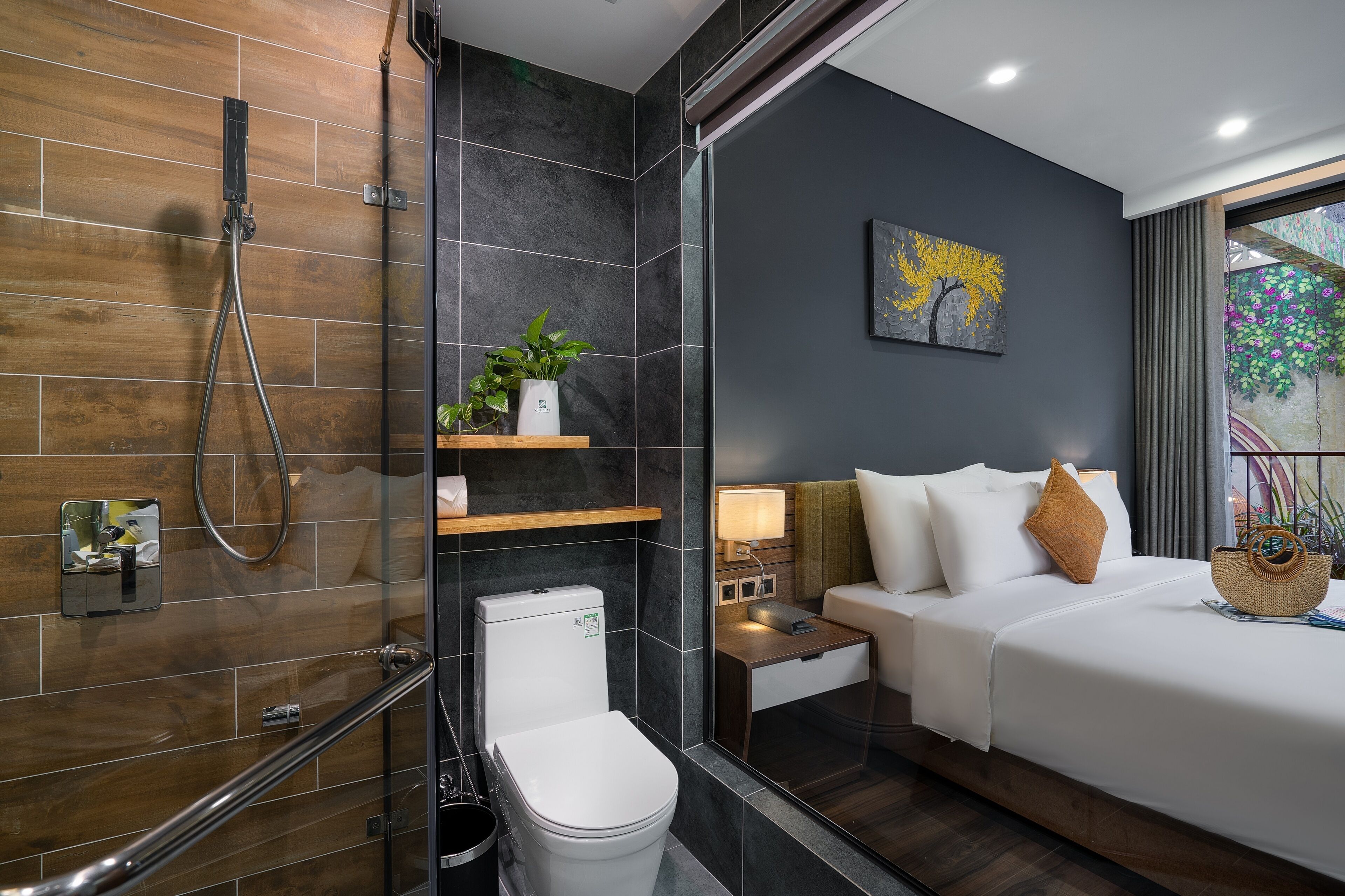 A modern bathroom with a glass shower enclosure, a toilet, and a bedside table with a lamp.