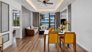 A modern hotel room with a dining area, a sofa, a ceiling fan, and a view of the outside. - Chi House Danang (Da Nang)
