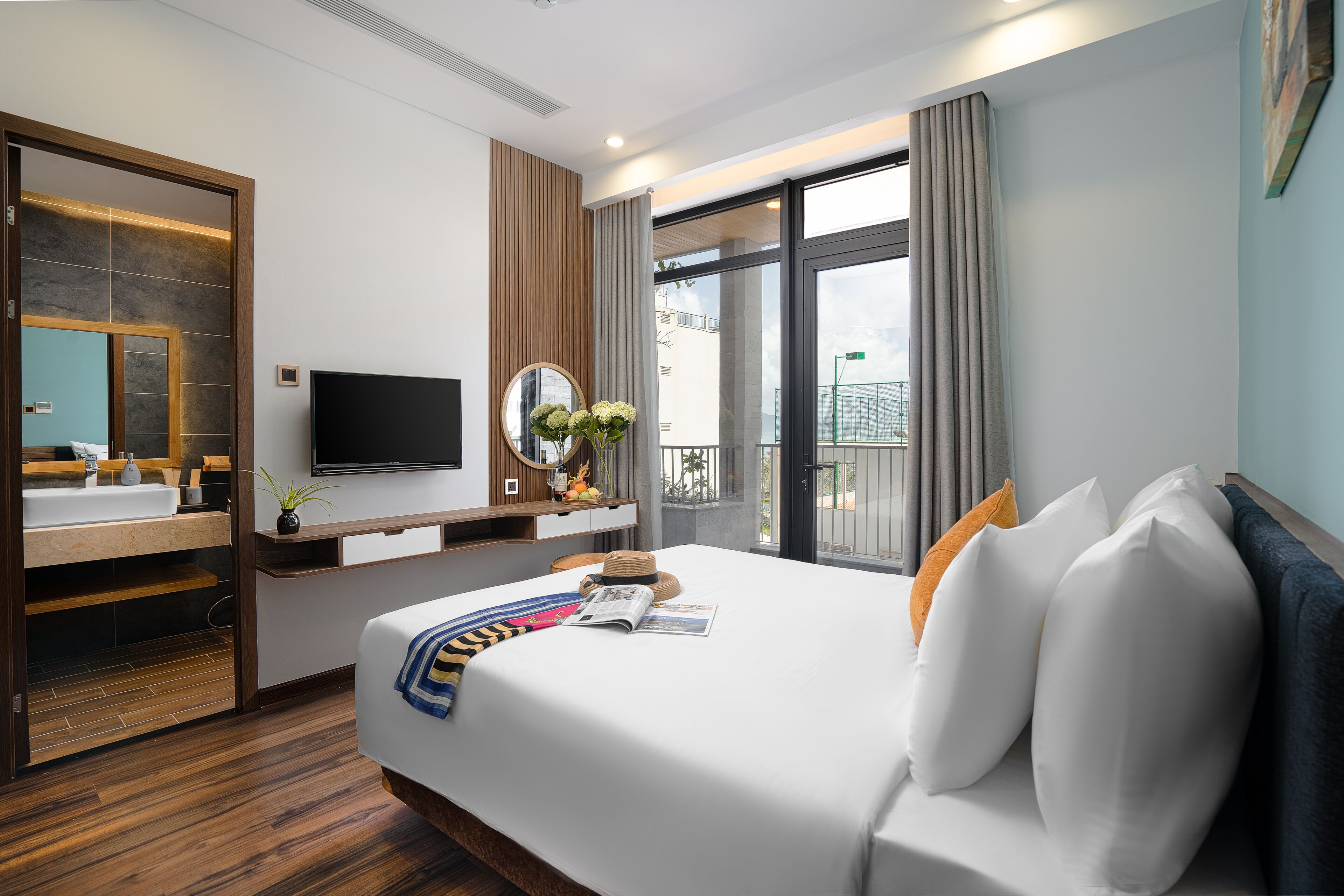 Una habitación de hotel moderna con una cama grande, televisión, baño con espejo y balcón con cortinas.