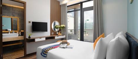 Una habitación de hotel moderna con una cama grande, televisión, baño con espejo y balcón con cortinas.