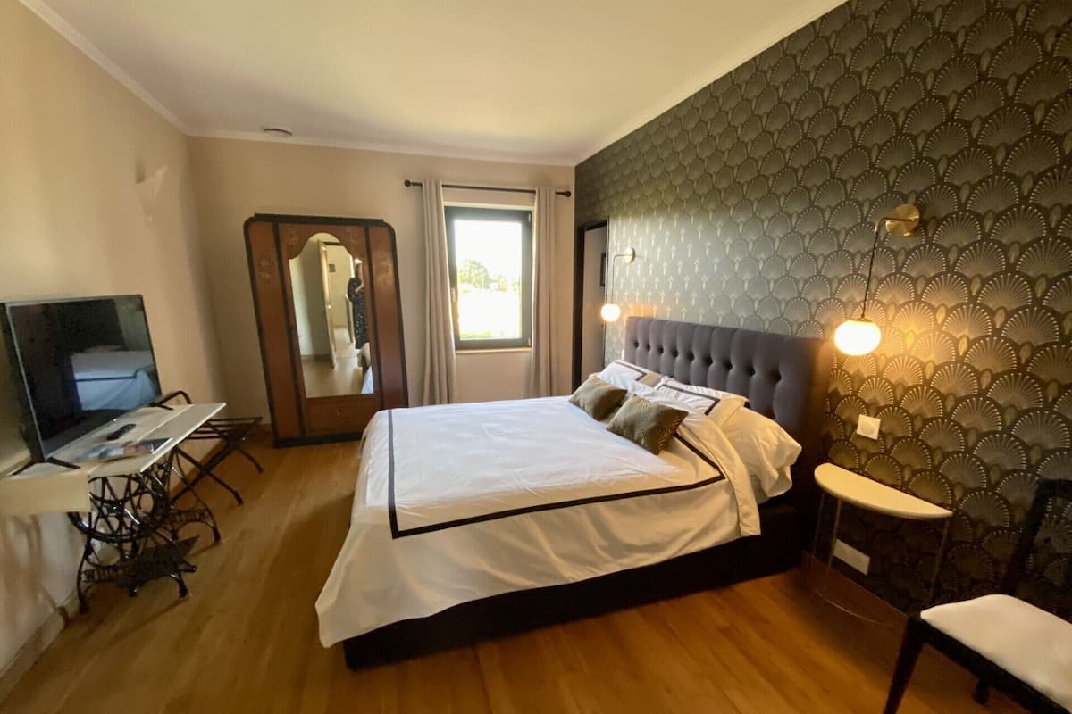 A bedroom with a large bed, a TV, a mirror, and a window.