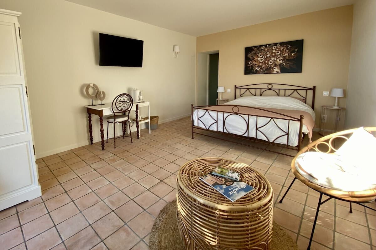 A bedroom with a bed, a desk with a chair, a television, and a wicker ottoman.