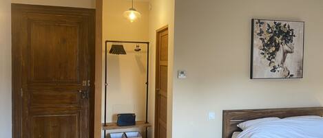 Une chambre avec une porte en bois, un lit avec une literie blanche, une petite table de chevet avec une lampe et une œuvre d’art accrochée au mur.