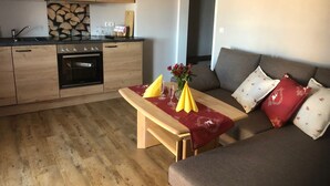Ein kompakter Wohnbereich mit einer Küchenzeile, einem Holzesstisch und einer Couch mit gemusterten Kissen.