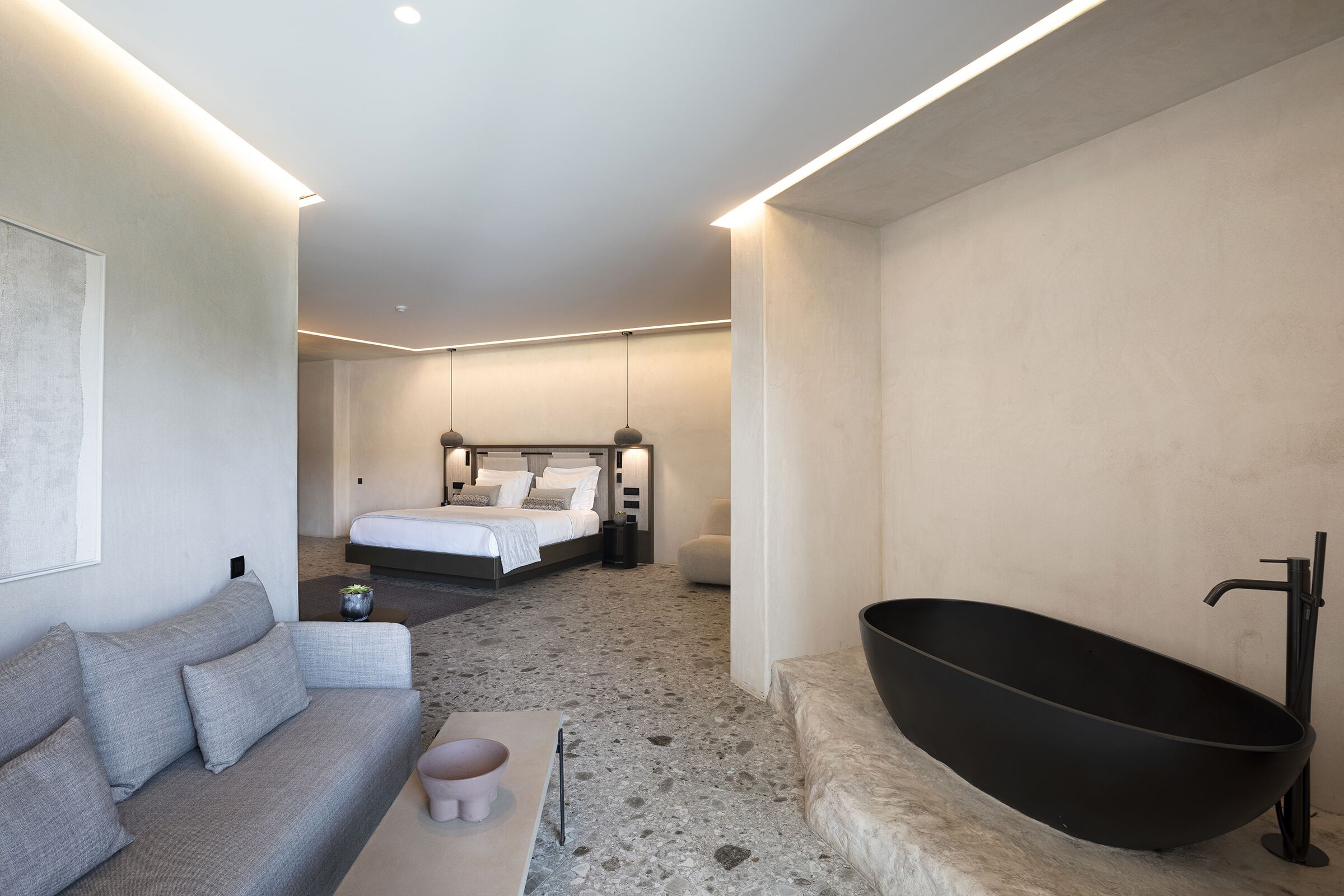 Una habitación de hotel moderna con una bañera grande, un sofá, una cama y un diseño minimalista.