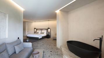 Una habitación de hotel moderna con una bañera grande, un sofá, una cama y un diseño minimalista.