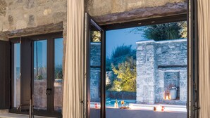 A modern outdoor space with a stone wall, a black bathtub, and a seating area with a plant. - Aeonic Suites and Spa (Mykonos)