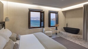 A modern bedroom with a large bed, a sitting area, a bathtub, and a view of the sea. - Aeonic Suites and Spa (Mykonos)