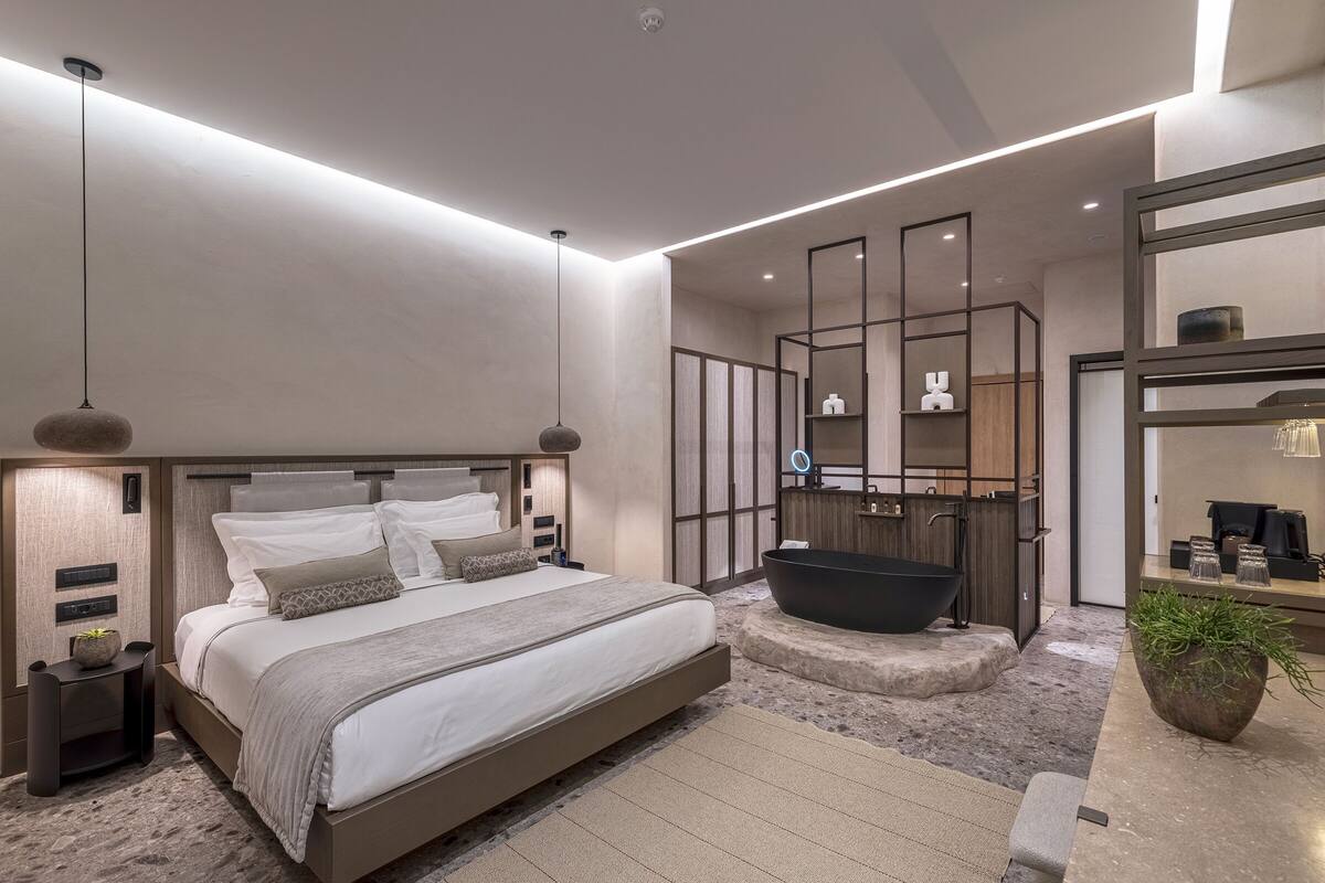 Un dormitorio moderno con una cama grande, una bañera integrada y un baño minimalista con un espejo grande y estanterías.
