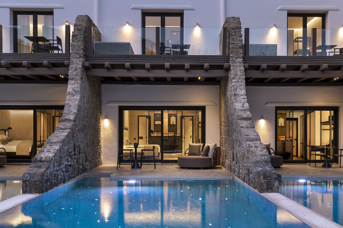 Un hotel moderno con piscina, mobiliario exterior y una entrada bien iluminada.