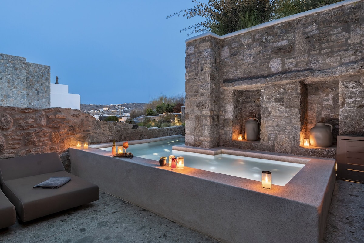 Un espacio al aire libre con paredes de piedra, una bañera de hidromasaje, velas y un sofá.