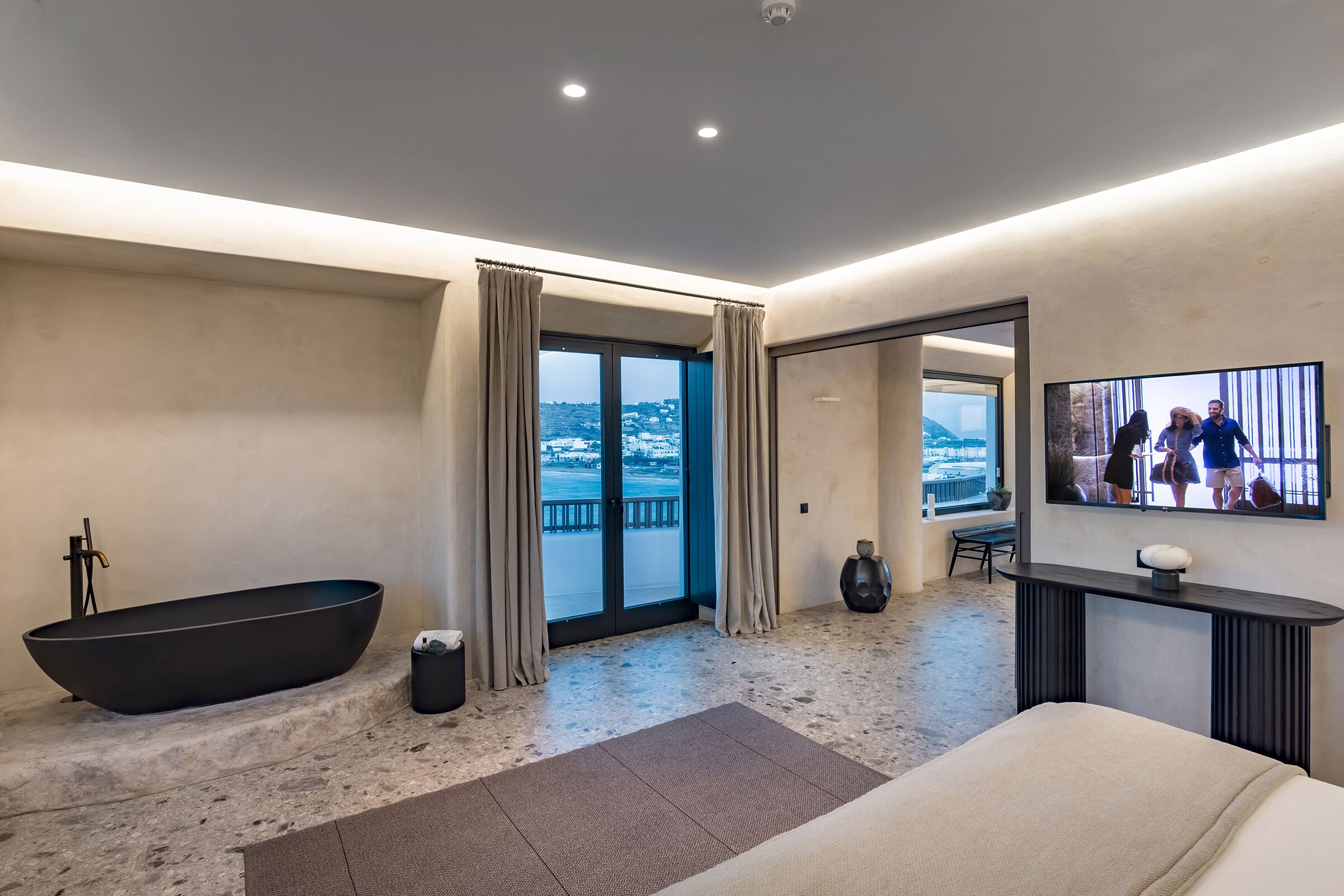 Ein modernes Badezimmer mit einer schwarzen Badewanne, einem großen Spiegel und Blick auf einen Balkon.