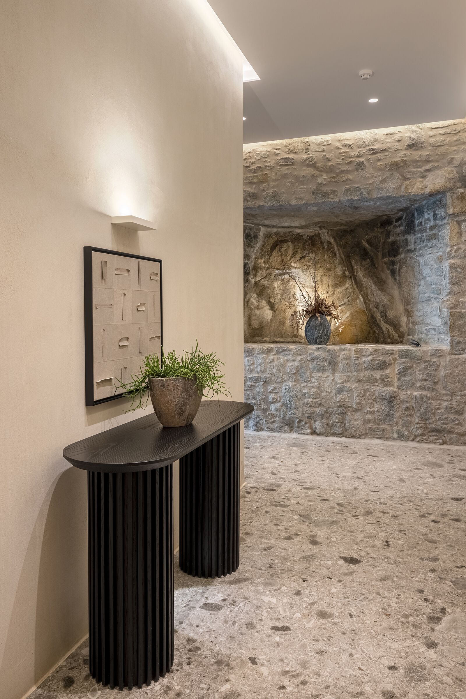 Un interior moderno con pared de piedra, una planta en maceta y una obra enmarcada sobre una consola.