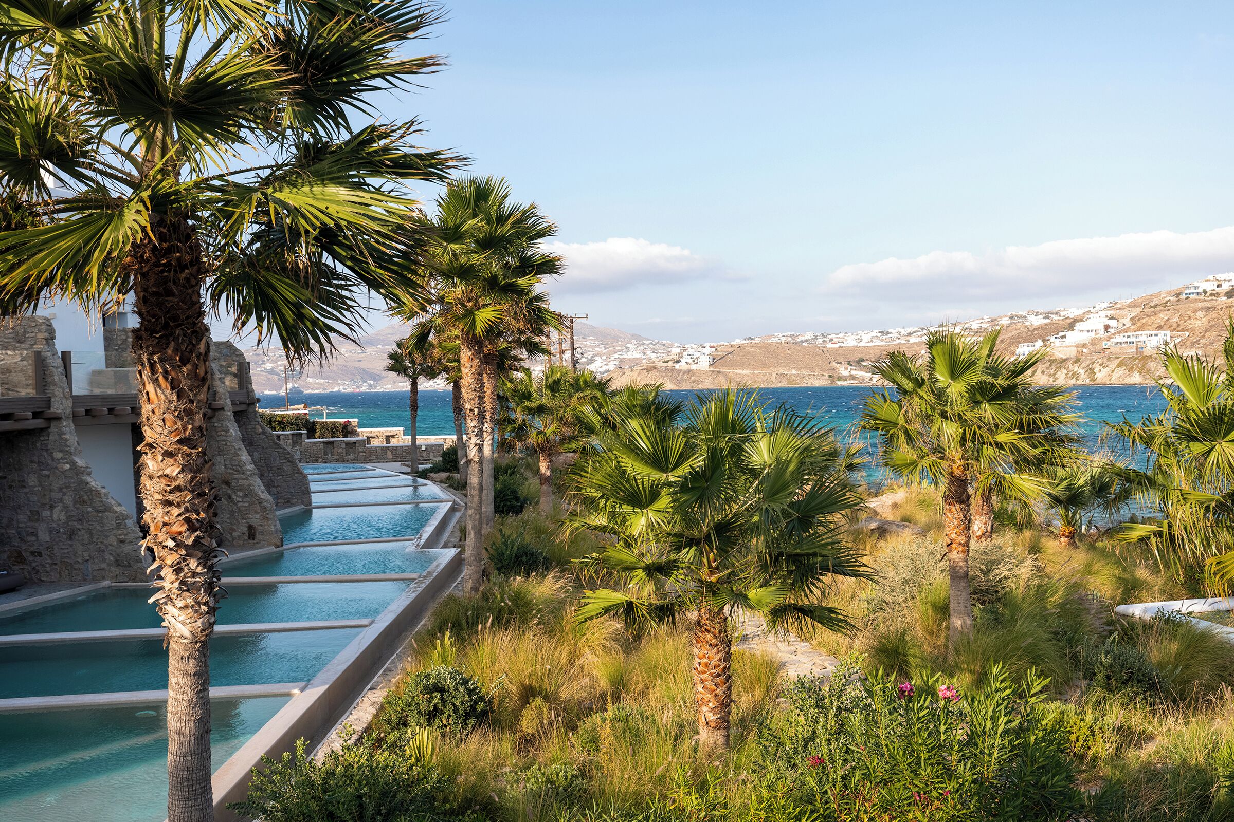 Zona de piscina con palmeras y vistas al mar y las colinas.
