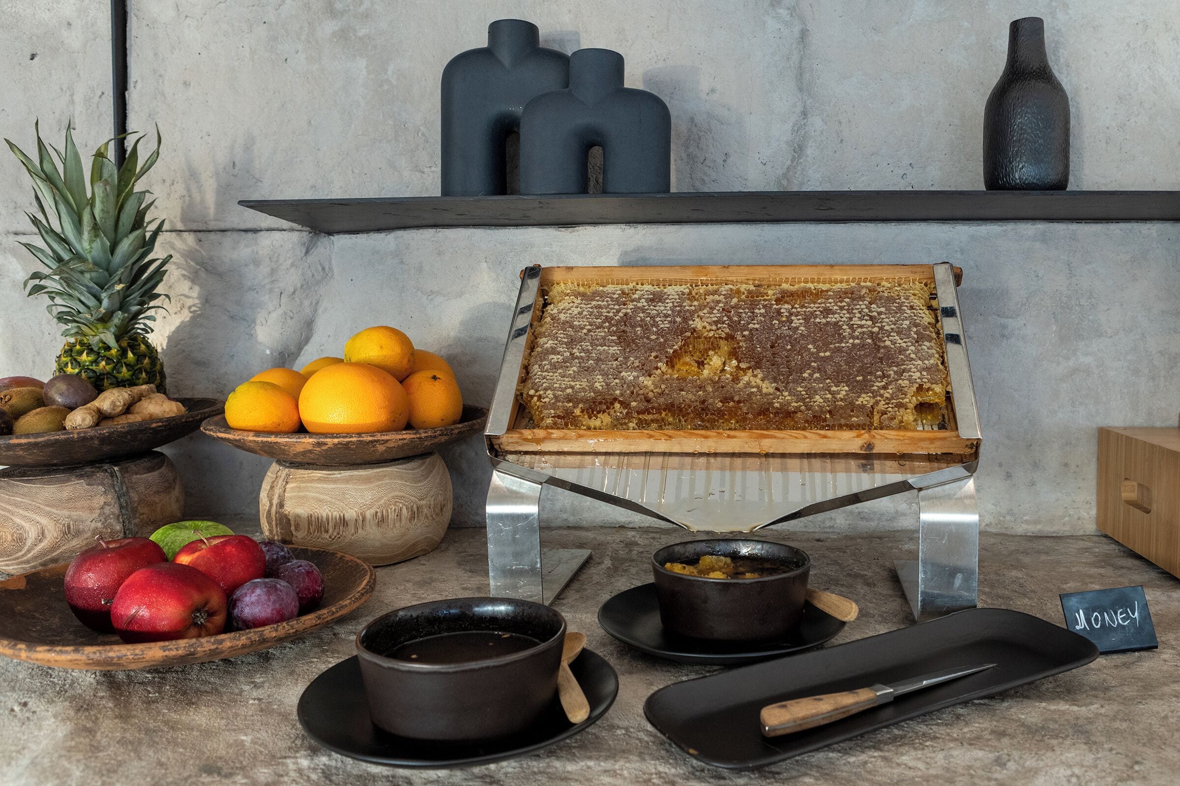 A kitchen counter with a honeycomb frame, bowls of fruits, and a honey jar.