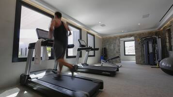 Un gimnasio con cintas de correr, una máquina de pesas y una pelota de ejercicios grande.