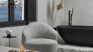 A modern bathroom with a large window, a bathtub, a towel, and a tray with food items. - Aeonic Suites and Spa (Mykonos)