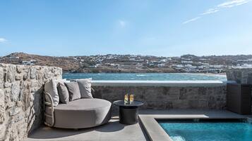 Un área junto a la piscina con un muro de piedra, una zona de estar con cojines y vistas a un pueblo costero.