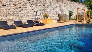 Une piscine aux eaux cristallines, bordée de chaises longues, avec un mur de pierre en arrière-plan.
