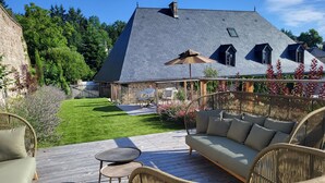 A patio with wicker furniture, a stone wall, and a lawn. - Gîte Haut de Gamme en Haute Corrèze (Meymac)