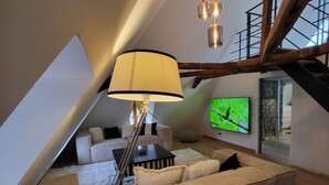 Un salon moderne avec un grand canapé d’angle, une lampe sur pied, un téléviseur à écran plat et un escalier.