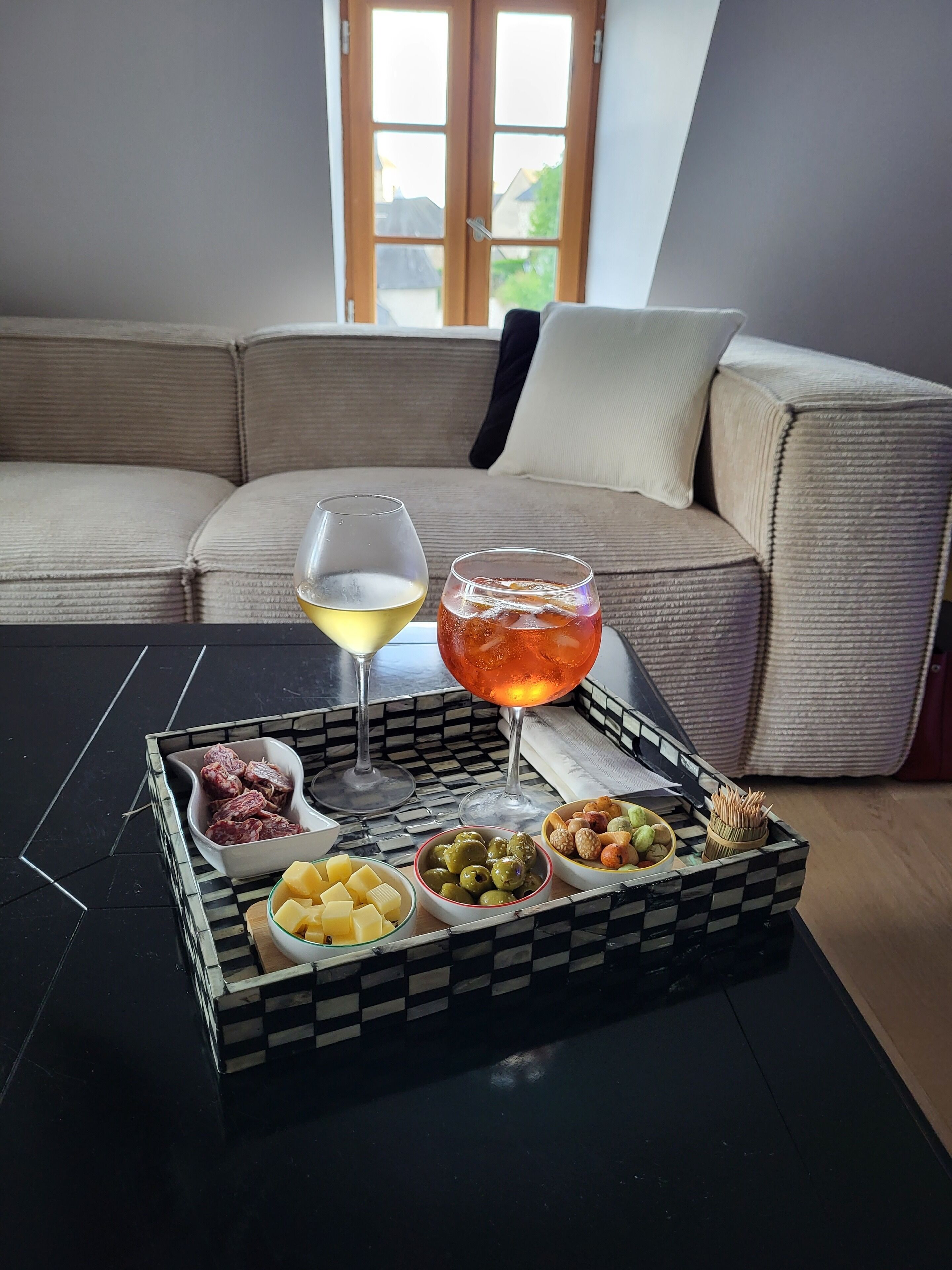A tray with food and drinks on a table in a living room with a sofa and a window in the background.