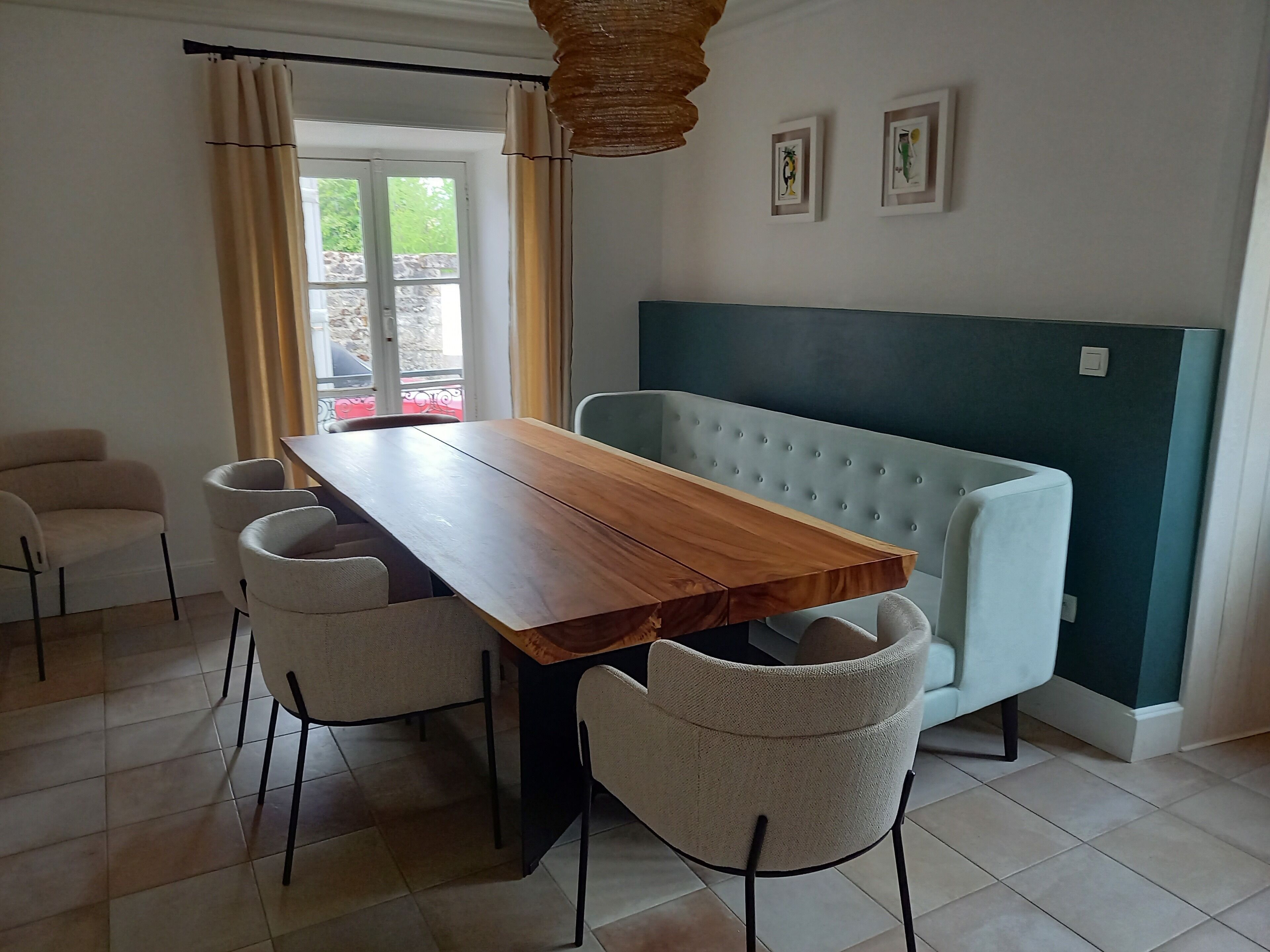 Een eethoek met een houten tafel en vier stoelen, een bank en een raam met gordijnen.