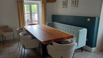 Een eethoek met een houten tafel en vier stoelen, een bank en een raam met gordijnen.